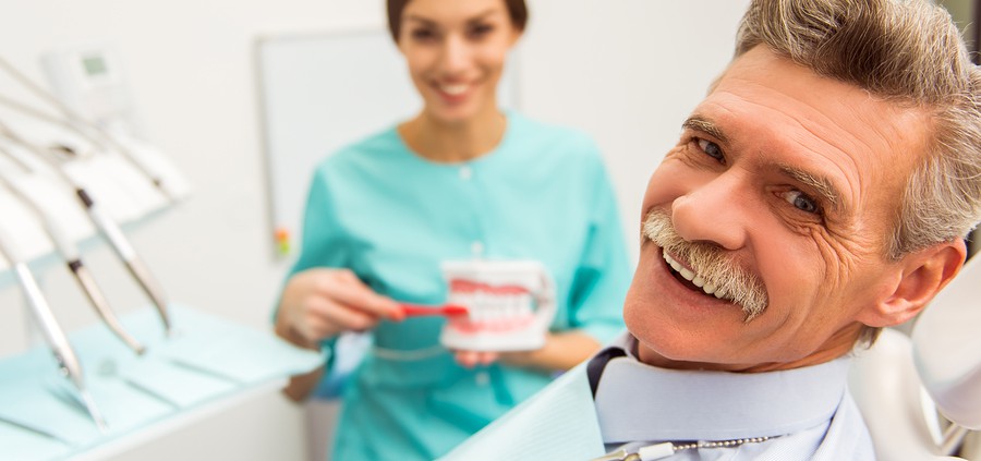 Older gentleman patient in dental practice with hygenist shoing how to brush dentures