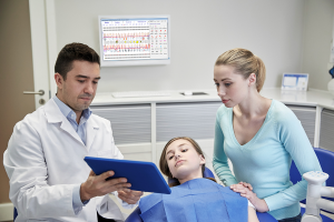 dentist and parent in exam room looking at an ipad as the child lays in the chair