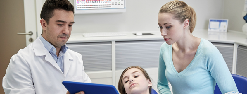 dentist and parent in exam room looking at an ipad as the child lays in the chair