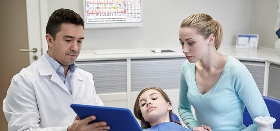 dentist and parent in exam room looking at an ipad as the child lays in the chair